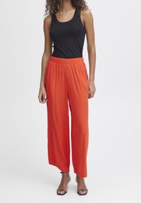 Röda vida byxor med texturerad yta och elastisk midja, tillsammans med en figurnära svart linne och svarta sandaler med remmar.