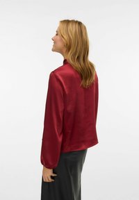 Bordeaux satijnen blouse met lange pofmouwen, hoge halslijn en een lichte glans. Zachte textuur, rechte snit en een relaxte pasvorm.