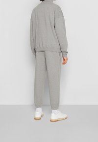 Sudadera gris y pantalones joggers a juego hechos de tela suave. La sudadera tiene un cuello alto; los joggers cuentan con puños elásticos y bolsillos laterales.