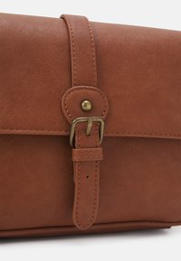 Brązowa skórzana torba o gładkiej fakturze, z zapięciem na mosiężną klamrę i przeszytymi brzegami. Zawiera element paska zapewniający bezpieczeństwo.