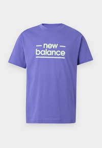 Μωβ κοντομάνικη μπλούζα με στρογγυλή λαιμόκοψη, με λευκό κείμενο "new balance" και λευκές γραμμές στο κέντρο μπροστά, σε απλό φόντο.