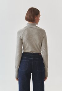 Maglione grigio a collo alto con texture a costine e spalle senza cuciture, abbinato a jeans alta vita blu scuro con tasche posteriori.