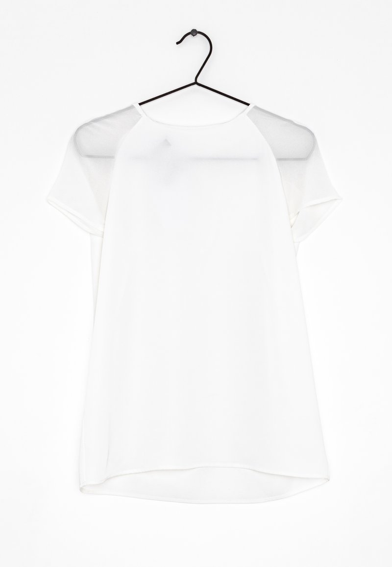 Haut blanc à manches courtes sur un cintre noir, présentant une texture lisse, une coupe décontractée et un col rond avec des accents transparents sur les épaules.