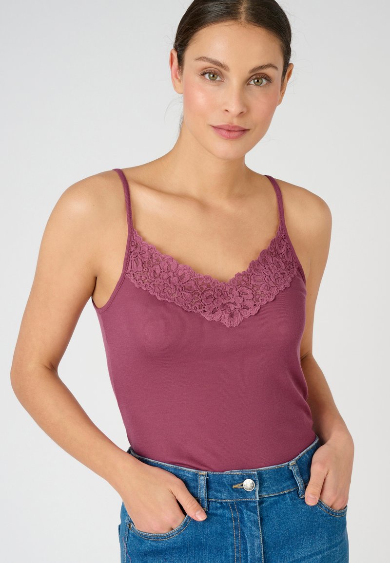 Mauve camisole with lace trim at the neckline, thin straps, made from a soft, stretchy fabric, paired with high-waisted denim.