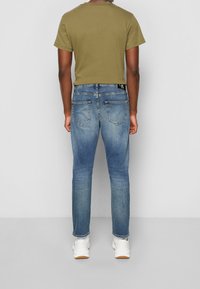 Olivgrön t-shirt med kort ärm, kombinerad med blå slimfit-jeans som har bakfickor, samt vita sneakers med en beige sula.