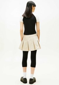 Zwart-wit aansluitend topje, beige geplooide rok, zwarte legging en dikke zwarte plateauzolen, met witte sokken zichtbaar bij de enkel.