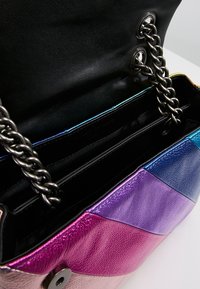 Farverig læderhandbag med en kædestropp, sort interiør og en livlig gradient af pink, lilla og blå på ydersiden.