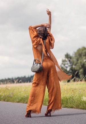 Hnědo-červený lněný oděv s širokými nohavicemi, otevřeným zadním dílem a detaily na zavazování; doplněný malou kulatou tmavě zelenou kabelkou a sandály na otevřenou špičku.