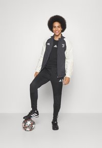 Schwarz-weißer Adidas Trainingsanzug mit Logo, schwarze Stiefel und ein Fußball; zeichnet sich durch kontrastierende Ärmelfarben und gestreifte Hosenakzente aus.