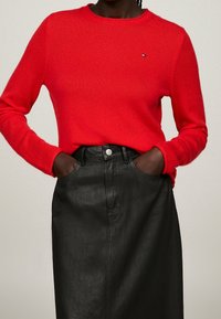 Roter Stricksweater mit Rundhalsausschnitt, kombiniert mit einem schwarzen Lederrock mit einer Fronttasche und silbernen Knopfdetails.