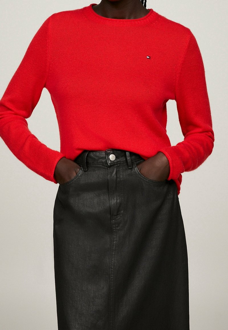 Roter Stricksweater mit Rundhalsausschnitt, kombiniert mit einem schwarzen Lederrock mit einer Fronttasche und silbernen Knopfdetails.