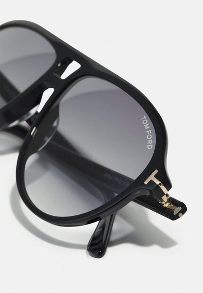 Ochelari de soare negri cu un finisaj lucios, având lentile cu gradient gri și un accent auriu distinctiv pe sprijin. Numele brandului "TOM FORD" este vizibil.