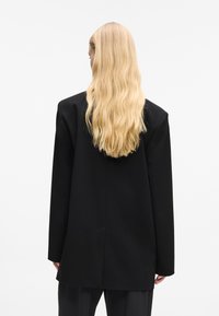 Melnā piegriezuma žakete ar strukturētu dizainu, ar garām piedurknēm, vienu aizmugures venti un gludu audumu.