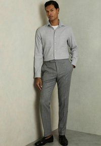 Grå skjorte med knapper, grå stribede bukser, sorte sko. Stoffet ser glat ud; skjorten har en brystlomme; tætsiddende silhuet.