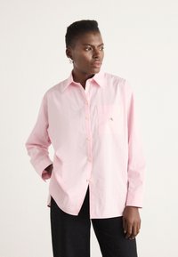 Ljust rosa långärmad skjorta med knappad krage, med bröstficka och broderad logga. Tillverkad av mjukt bomullstyg.
