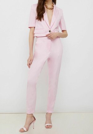 Costume rose clair sur mesure avec un blazer court, fermeture à un bouton et pantalon assorti ajusté. Tissu lisse au design minimaliste.