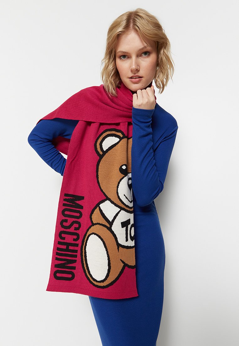 Strickschal in kräftigem Pink und Beige, mit einem Cartoon-Bären-Motiv. Der Text "MOSCHINO" ist zusammen mit dem Bären-Design auffällig platziert.