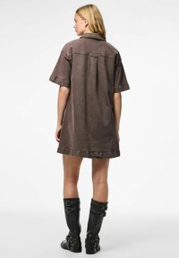 Robe en denim marron à manches courtes, avec un col rabattable et des poches latérales, associée à des bottes noires à boucles hauteur genou.