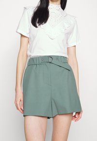 T-shirt bianco in cotone con colletto in pizzo a taglio; abbinato a pantaloni corti alti di colore verde menta con cintura e tasche davanti.