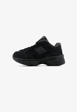 Basket sportive noire avec semelle épaisse, dessus en mesh et en suède, laçage et logo de marque sur le côté sur fond blanc.