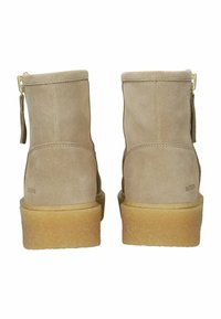 Botas de tobillo de ante beige con un cierre lateral y una suela de goma de color miel. Presentan una textura suave y una marca mínima en el talón.