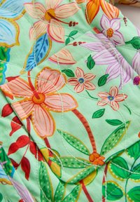 Prošívaná látka se světle zeleným pozadím zdobeným barevnými květinovými vzory v růžové, oranžové, fialové a modré barvě, doplněná zelenými listy.