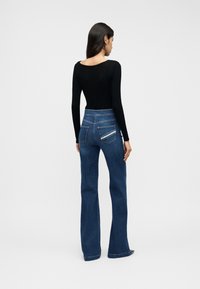 Μαύρο τοπ μακρυμάνικο και ψηλόμεσα, φαρδιά μπλε τζιν με τσέπες στο πίσω μέρος και αντίθετη ραφή. Ομαλή υφή, εφαρμοστό σχέδιο.