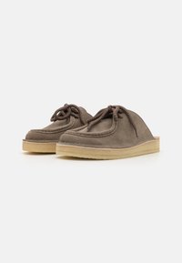 Scarpe slip-on in suede marrone con forma arrotondata, caratterizzate da lacci marroni e una suola in gomma chiara. Texture morbida e design minimal.