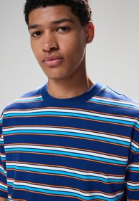 Blåstribet t-shirt med horisontale striber i lyseblå, orange og hvid, med rund halsudskæring og korte ærmer. Blød stofstruktur.