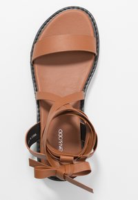 Ruske nahkate sa sandali z tremi trakovi, ravnim podplatom in zvitim trakom na strani. Teksturni notranji del in črni rob podplata.