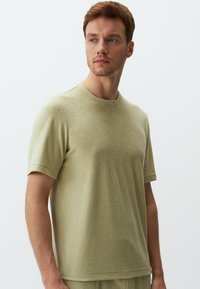 Jasnozielona bluzka z krótkim rękawem wykonana z miękkiego materiału, z okrągłym dekoltem i luźnym krojem. Brak widocznych wzorów lub ozdób.