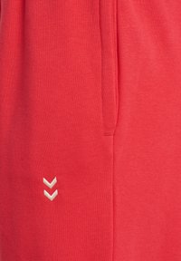 Zbliżenie czerwonej tkaniny z dwoma małymi białymi skierowanymi w dół esami ujarzmionymi blisko pionowego szwu lub kieszeni.