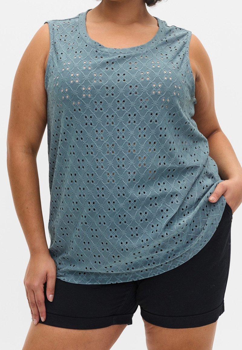 Haut sans manches en sarcelle avec un motif ajouré texturé. Dispose d'un col arrondi et d'une coupe ample, porté avec un short noir.