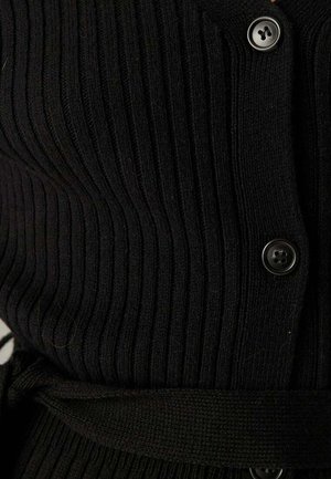 Nærbillede af sort ribstrikket stof med sorte knapper og et detaljeret bindebånd.