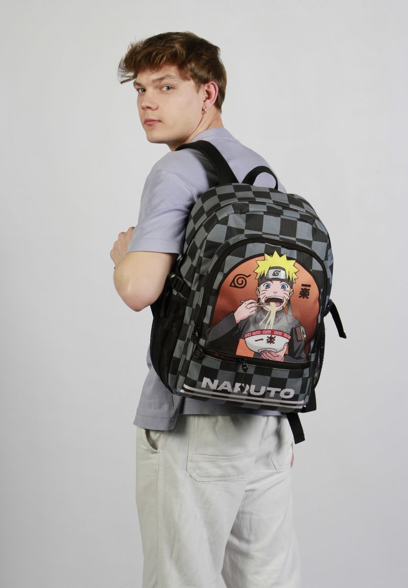 Sac à dos à carreaux noir et gris avec une illustration d'un personnage de Naruto, portant un logo bien en vue en bas. Tissu texturé, bretelles ajustables.