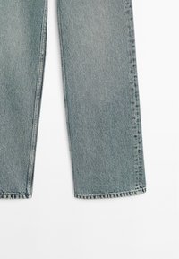 Jeans in denim azzurro chiaro con vestibilità rilassata, gambe dritte e cuciture visibili. Il tessuto ha una texture morbida e una leggera sbiaditura.