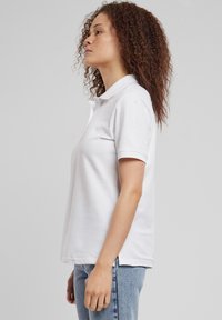 Bijela polo majica s klasičnim ovratnikom i kratkim rukavima, izrađena od pamuka. Krojenje je opušteno, upareno s trapericama svijetlog pranja.