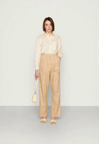 Camisa botonê de padrão amarelo claro combinada com calças largas de cintura alta beige. Os acessórios incluem uma pequena bolsa amarela e sandálias combinando.