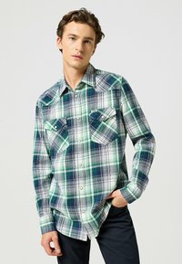Koszula w kratę z długim rękawem w zielonym, granatowym i białym kolorze, z dwoma kieszeniami z przodu, kołnierzykiem w szpic i zapięciem na guziki. Wykonana z lekkiego materiału.