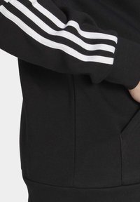 Black sweatshirt featuring white stripes on the sleeves, ribbed cuffs, and a kangaroo pocket, with a soft, textured fabric.