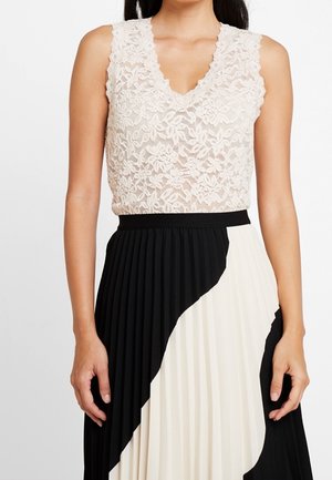 Mouwloze witte kanten top met bloemenpatroon, gecombineerd met een hoog uitgesneden geplooide rok in zwart-wit kleurblok.