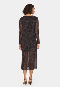 Long-sleeve, sheer black dress with a leopard print pattern, featuring a straight cut and hemline at mid-calf. Worn with green heeled sandals.