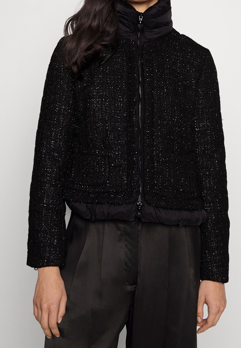 Black, cropped jacket combines textured woven fabric with a puffy, quilted black collar and bottom hem. Features a central zipper.