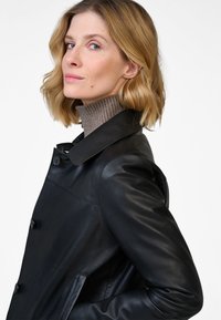 Black leather coat with a collared neck, featuring button closures and side pockets. Smooth texture and tailored fit.