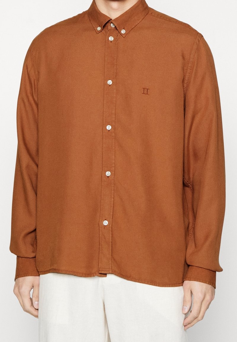 Camicia marrone a maniche lunghe con colletto a punta, caratterizzata da bottoni bianchi e ricami sottili. Tessuto liscio e vestibilità rilassata.