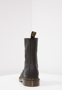 Botte mi-mollet en cuir noir avec couture jaune sur la semelle, semelle brune translucide et boucle de talon en tissu noir avec texte jaune.
