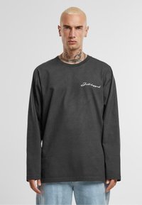 Langærmet, mørkegrå t-shirt lavet af bomuld, med et hvidt kursiv logo på brystet og en afslappet pasform med rund halsudskæring.