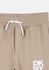 Beige sweatpants met geribbelde elastische tailleband, witte koord geknoopt, en witte DKNY-logo aan de rechterkant van de voorkant.