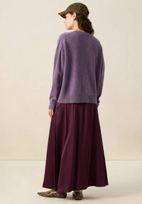 Pull violet surdimensionné avec ourlet côtelé, associé à une jupe maxi bordeaux fluide. Casquette à imprimé léopard et chaussures à motifs complètent le look.