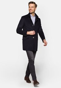 Granatowy wełniany płaszcz z klapami, dwoma przednimi kieszeniami i zapięciem na guziki, zestawiony z szarymi dżinsami i brązowymi butami. Pod spodem widoczna paskowana koszula.